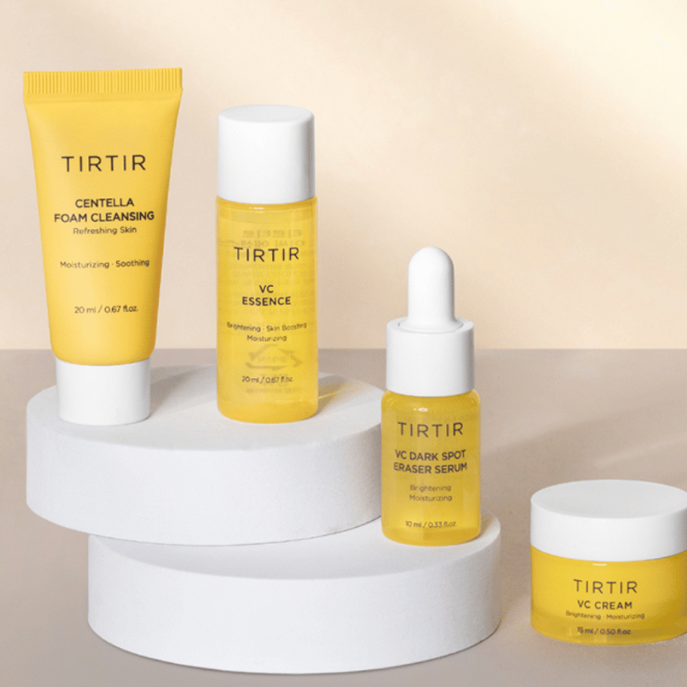 Ett kit med Tirtirs VC-produktlinje visas på en ljus bakgrund. Kitet innehåller fyra produkter: "Centella Foam Cleansing" i en gul tub, "VC Essence" i en transparent flaska, "VC Dark Spot Eraser Serum" i en gul droppflaska och "VC Cream" i en gul krämburk.